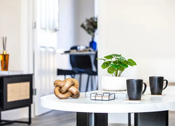 A white table with a pretzel, a plant, and two cups on it.